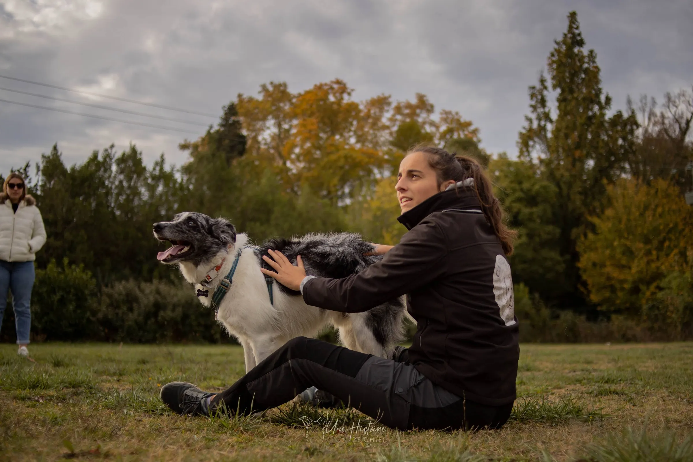 Inès assise dans l'herbe avec son chien portant un harnais, éducation canine bienveillante
